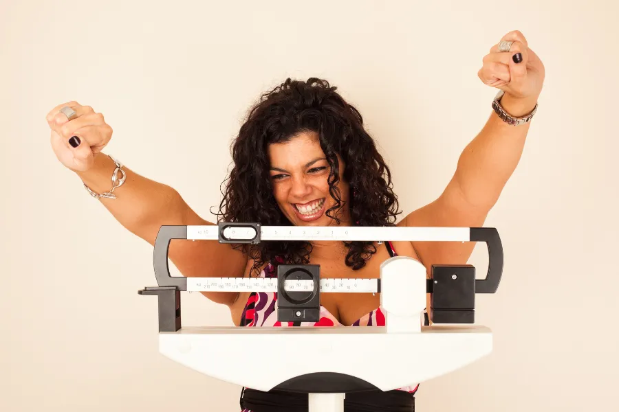 Woman looking at scale raising her arms in joyous manner
