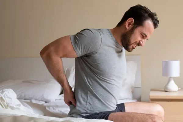 Man sitting up in bed holding his lower back