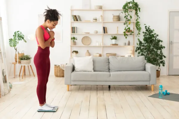 Woman standing on scale, dressed in exercise clothes standing in living room