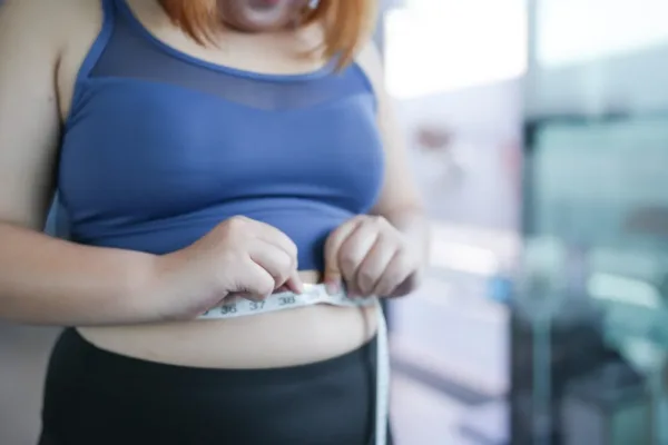 Woman wearing tank top measuring her mid section with a tape measure