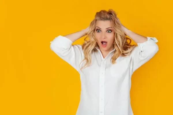 Woman on orange background with hands on head