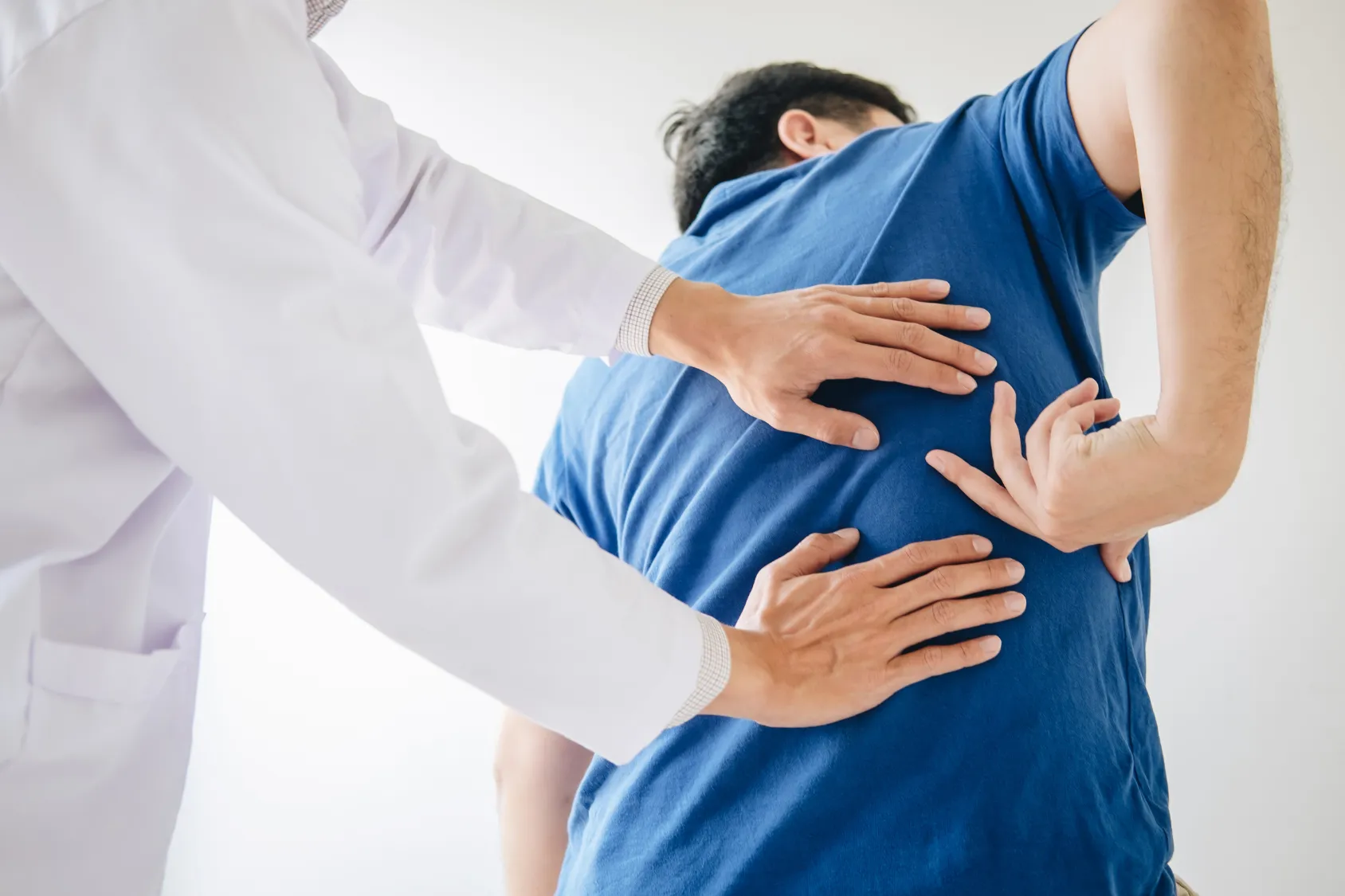 Doctor assessing a patient’s lower back during a physical exam.