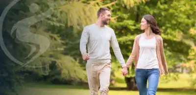 Couple holding hands walking on outdoor path. Sano Logo on left side with low opacity